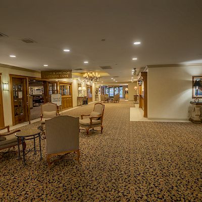 A hotel lobby featuring seating arrangements, wall art, a carpeted floor, and various signs leading to different amenities and areas within the hotel.