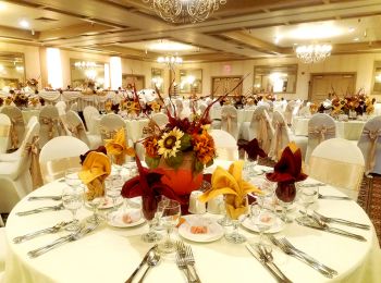 A banquet hall with elegantly set tables, adorned with floral centerpieces and ornate chandeliers overhead, ready for a special event.