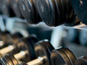 The image shows a rack of black dumbbells, commonly used for weight training in a gym or fitness center.