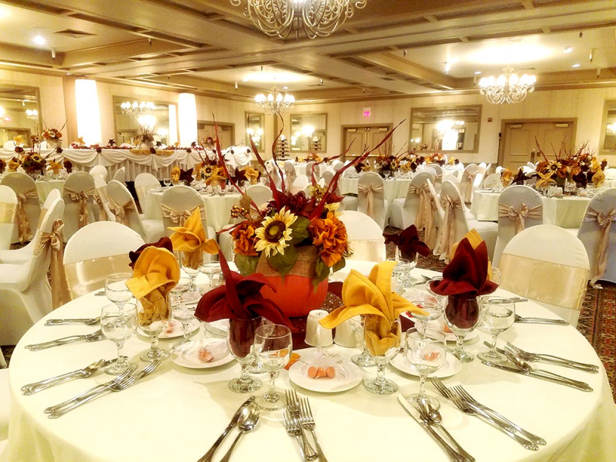 The image shows a beautifully decorated event hall with round tables set for a formal occasion, complete with floral centerpieces and neatly arranged cutlery.