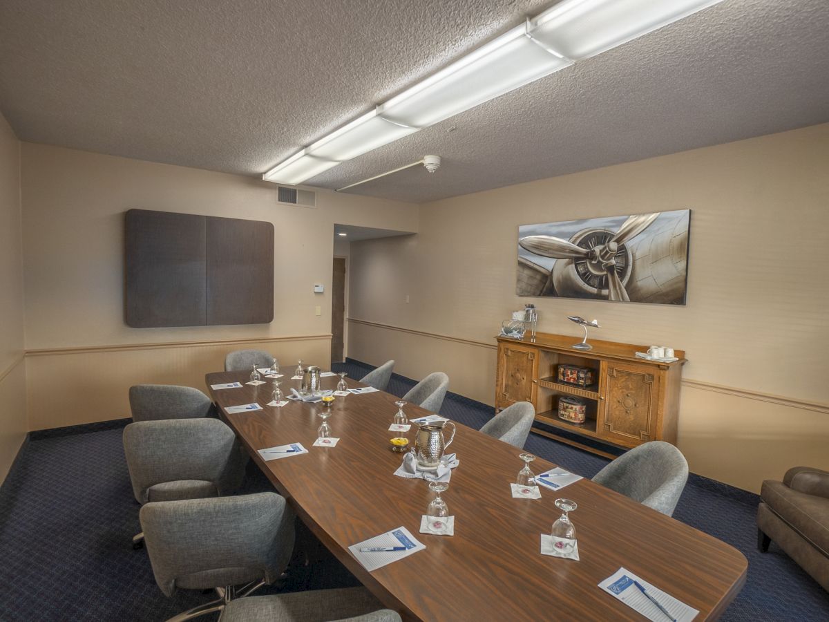 A conference room with a long table, surrounded by chairs, set up with water bottles and notepads, and a painting and cabinet at the back.