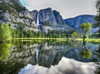 A serene landscape featuring a waterfall cascading down a mountain, lush greenery, and a clear lake reflecting the scenery, set amidst towering cliffs.