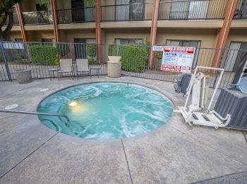 The image shows a fenced outdoor hot tub with bubbling water, a handrail, poolside chairs, and a lift for accessibility.