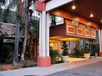 The image shows the entrance of a commercial building, possibly a hotel, with a covered driveway, potted plants, and exterior lighting for decoration.