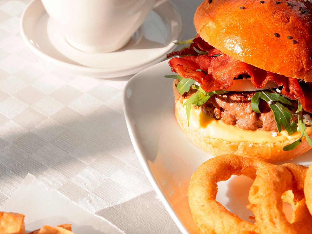 The image shows a meal with a burger, onion rings, nachos with dip, and a cup of coffee on a white tablecloth.