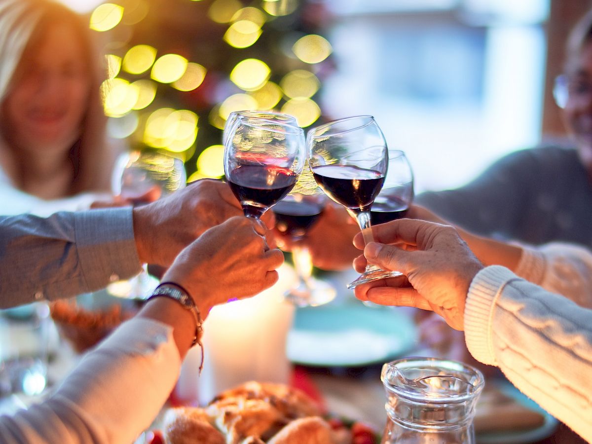 People are toasting with wine glasses around a table set with candles, food, and festive decorations, likely during a holiday celebration.