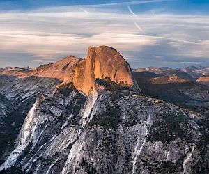 The image shows a stunning view of Half Dome, a prominent rock formation in Yosemite National Park, with surrounding mountains and a partly cloudy sky.